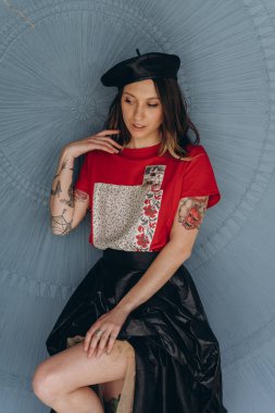 Kollarında dövmeleri olan, kırmızı bluz ve siyah etek giymiş, mavi arka planda poz veren arsız kız manzarası.