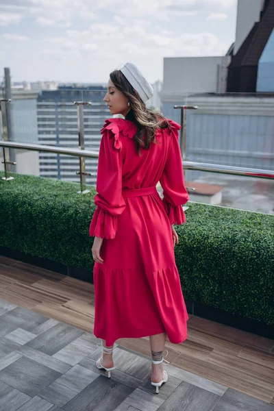 fashion photo of a glamorous woman dressed in a designer dress with a bright collar and white hat posing outdoor on a terrace