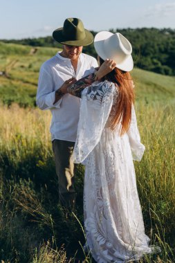 Happy young family spending  time together in nature, beautiful woman in white guipure dress with husband and their daughter walking  in the field