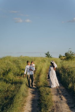Happy young family spending  time together in nature, the man holding his daughter and walking with his beautiful wife in the field