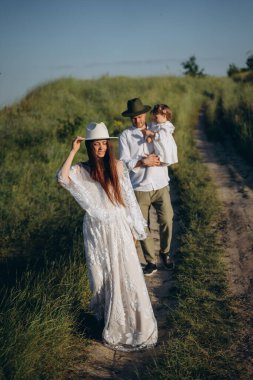 Happy young family spending  time together in nature, the man holding his daughter and walking with his beautiful wife in the field