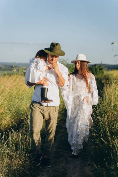 Happy young family spending  time together in nature, the man holding his daughter and walking with his beautiful wife in the field