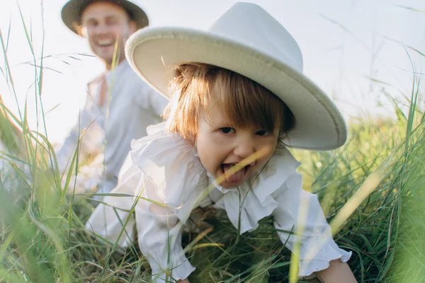 Happy young family spending  time together in nature, beautiful woman in white guipure dress with husband and their daughter sitting in the field