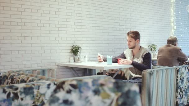Молодой человек со смартфоном сидит в кафе, крупным планом — стоковое видео