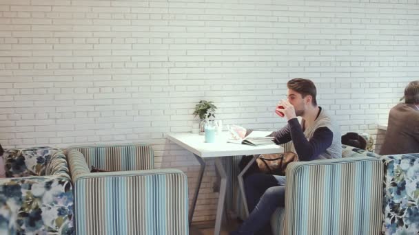 Joven con teléfono inteligente sentado en la cafetería — Vídeo de stock