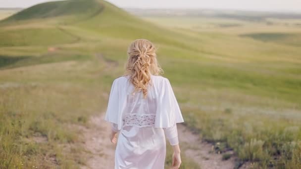 Женщина в белом платье гуляет по полю — стоковое видео