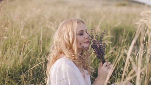Dziewczyna siedzi w trawie i pachnący kwiat — Wideo stockowe