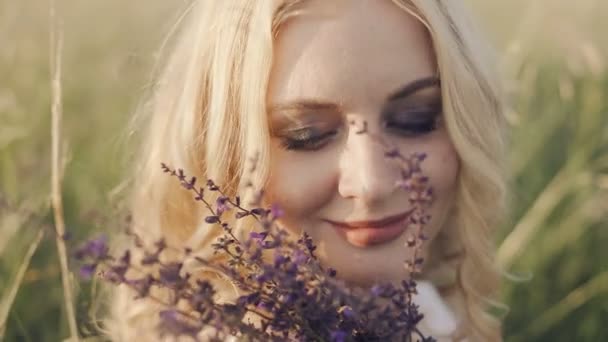 Fille blonde aux yeux bleus sentant un bouquet d'herbes — Video