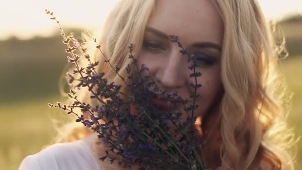 Девушка сидит в траве и нюхает цветок — стоковое видео
