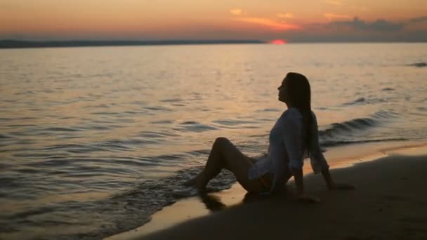 Flicka sitter på stranden på kvällen — Stockvideo