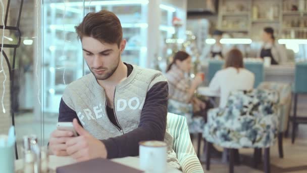 Молодой человек со смартфоном сидит в кафе — стоковое видео