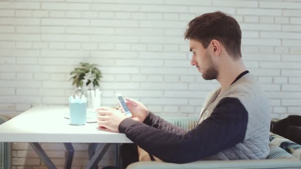 Молодой человек со смартфоном сидит в кафе — стоковое видео