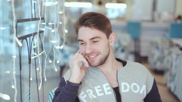 Щасливий молодий чоловік розмовляє по мобільному телефону і посміхається в кафе — стокове відео