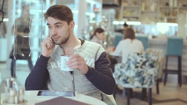Молодой человек разговаривает по мобильному телефону в кафе — стоковое видео