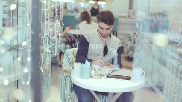 Молодой человек пишет в блокноте в кафе, стационарный снимок — стоковое видео