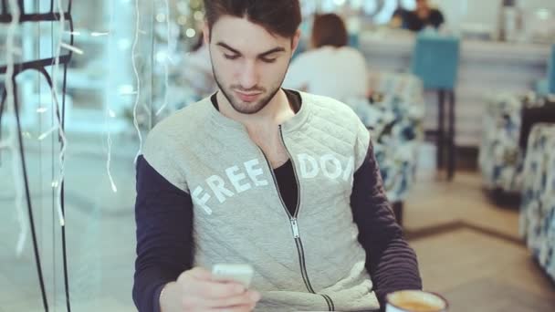 Joven con smartphone sentado en la cafetería, primer plano — Vídeo de stock