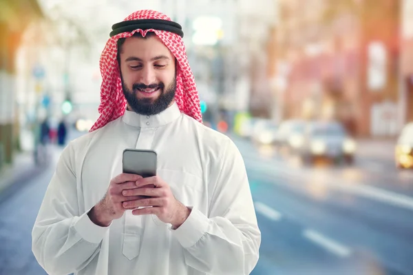 Hombre de negocios árabe trabajando con su teléfono en una calle llena de gente en el fondo — Foto de Stock