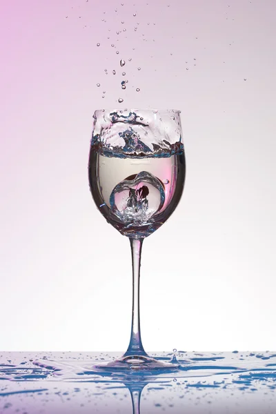 La caída de la uva en una copa de vino con salpicaduras de agua en el gradiente de rosa a blanco . — Foto de Stock