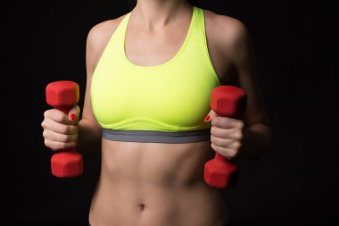 A yakın çekim sportif bir kadın elinde kırmızı bir dumbbells ile spor neon sarı sutyen giyiyor muscullar midesi olan.