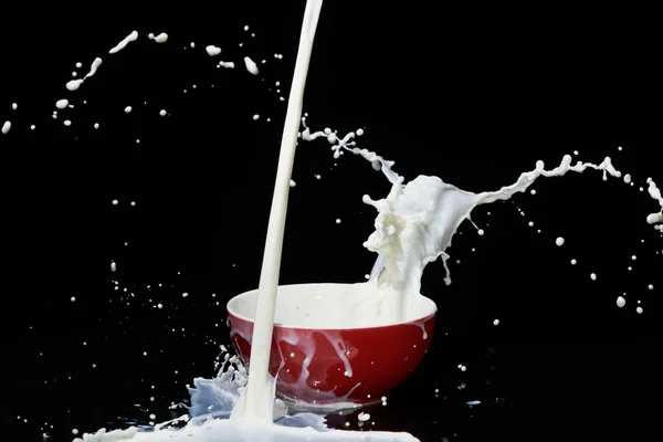 Падение потока молока рядом с красной чашей создает много всплесков и завихрений . — стоковое фото