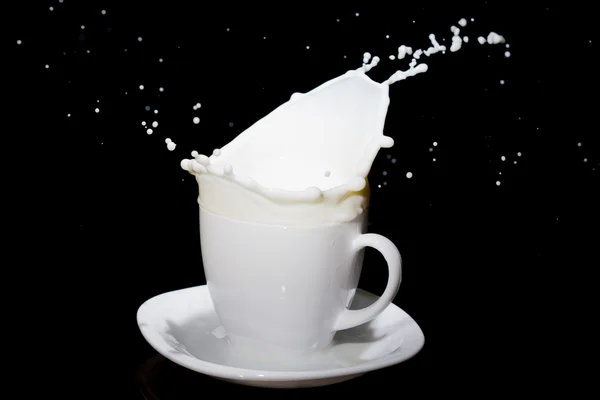 Spritzer Milch in weißer Teetasse stehen auf weißem Teller. — Stockfoto