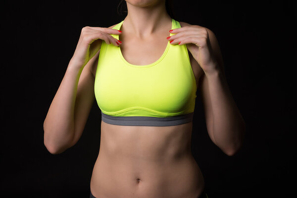 A close up of a sporty woman with a muscular stomach wearing sports touching by hands neon yellow bra.