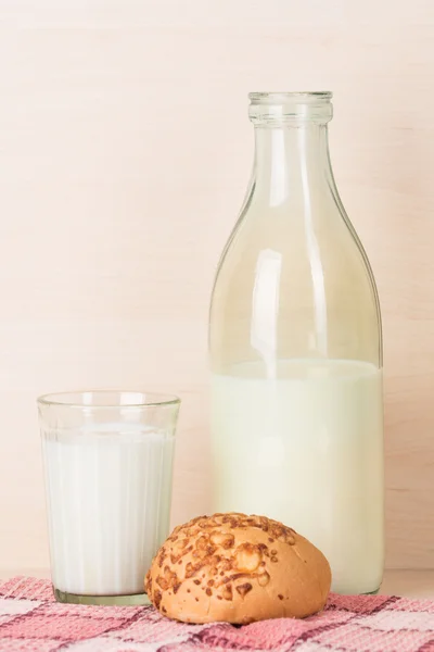 Garrafa de leite aberta à moda antiga com vidro facetado de leite e um pão em uma toalha de cozinha quadrada vermelha . — Fotografia de Stock