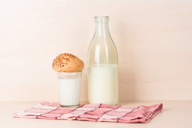 Yönlü bir bardak süt ile bir çörek bir geleneksel açılan eski moda şişe süt yakınındaki bir kırmızı kare mutfak havlu üzerinde duruyor.