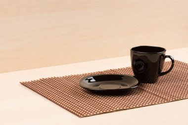 Black plate standing near black tea cup on tablemat. clipart