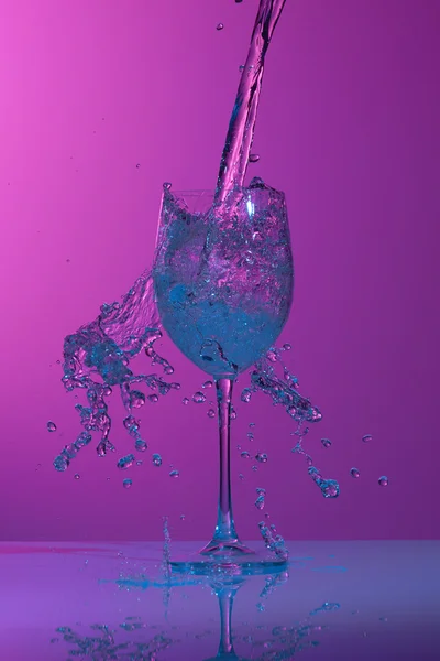 Caída de flujo de agua con tinte azul en la copa de vino creando muchas salpicaduras . — Foto de Stock