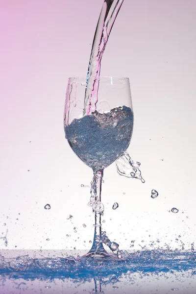 Agua con tinte rosado vertiendo en una copa de vino de gran tamaño con muchas salpicaduras . — Foto de Stock