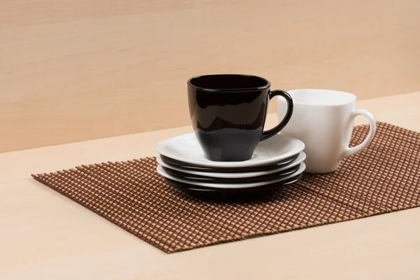 Black tea cup on the stack of the white and black plates near white tea cup on tablemat.