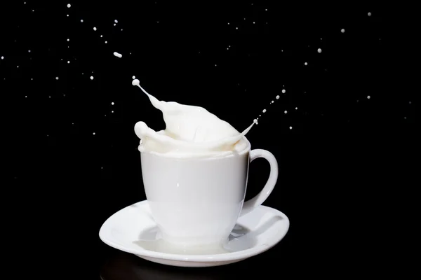 Milk with splashes in white tea cup standing on white plate. — Stock Photo, Image