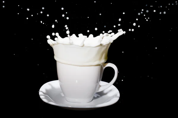 La leche en movimiento hace muchos salpicaduras en taza de té blanco de pie en el plato blanco . —  Fotos de Stock