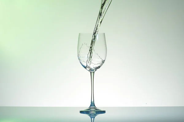 Agua que vierte en una copa de vino creando remolinos y salpicaduras . — Foto de Stock