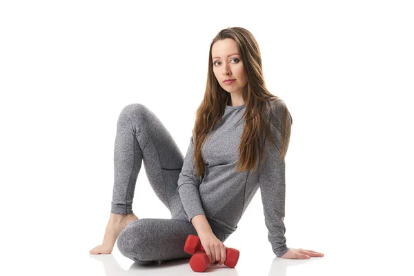 Attractive woman in sitting position two red dumbbells keeping in one hand in gray thermal underwear. — Stock Photo, Image