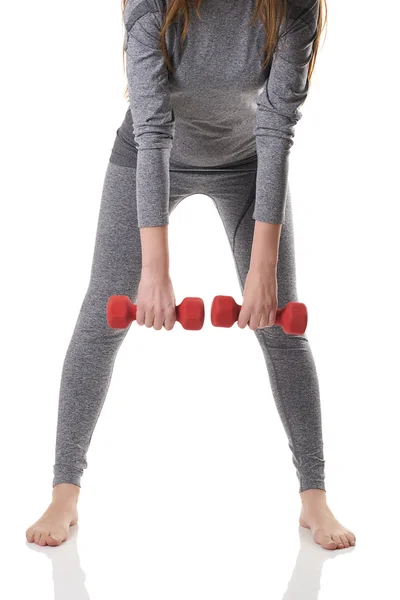 A woman body bellow shoulders level in gray sports thermal underwear doing exercises leaning forward using red dumbbells. Royalty Free Stock Photos