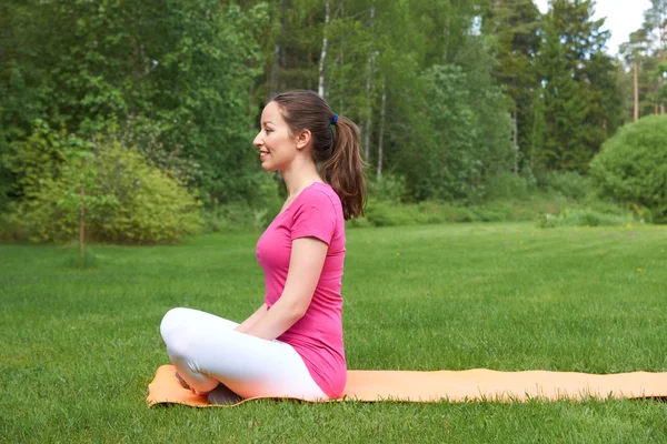 Gelukkig mooi bruin donkerharige vrouw mediteren op oranje mat in buiten in de natuur. — Stockfoto