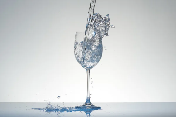 Agua con tinte azul vertiendo en una copa de vino con salpicaduras . — Foto de Stock