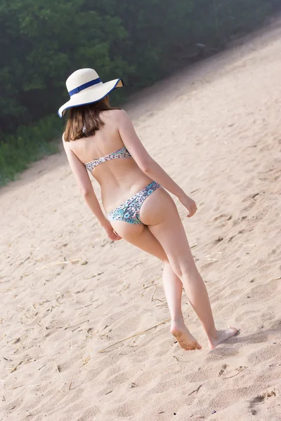 Сексуальная брюнетка в бикини с шапкой, идущая по песку у моря . — стоковое фото