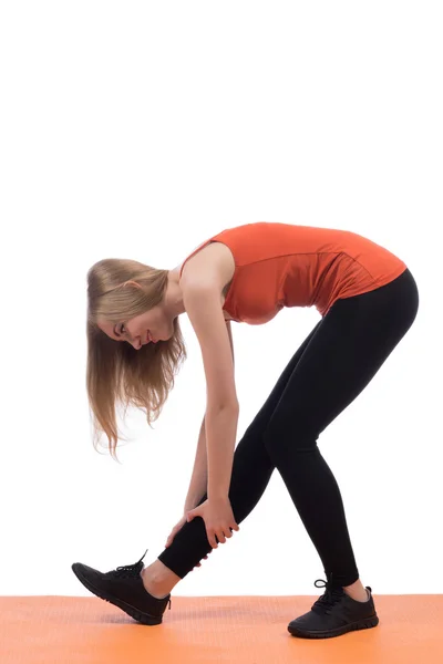 Mujer joven en entrenamiento de ropa deportiva espalda y pierna en una estera —  Fotos de Stock