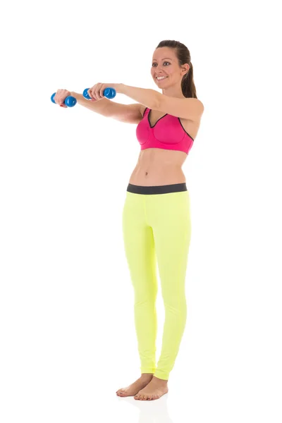 Mulher morena sorridente em esportes néon amarelo leggings e sutiã rosa fazendo exercícios complexos para os músculos das mãos usando halteres azuis — Fotografia de Stock