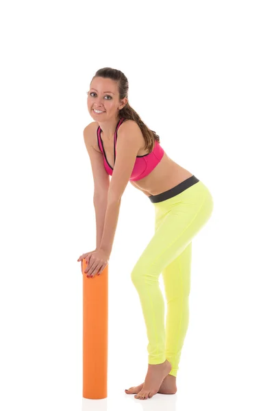 Mujer morena sonriente en polainas deportivas de neón amarillo y sujetador rosa apoyado en la esterilla naranja enrollada — Foto de Stock