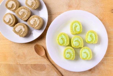 Tahta arka planda kaşıkla beyaz tabakta kremalı kek ve kahveli kek.