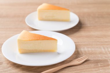 Beyaz tabakta çatallı vanilyalı cheesecake dilimi.