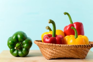 Taze kırmızı, bambu sepetinde sarı dolma biber ve ahşap tahtada yeşil dolma biber, renkli arka plan, organik sebzeler.