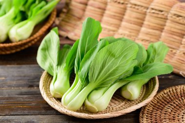 Tahta arka planda bambu sepeti içinde taze Bok Choy veya Pak Choi (Çin lahanası), organik sebzeler