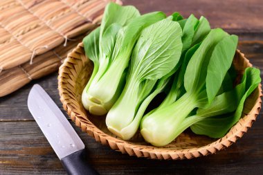 Tahta arka planda bambu sepeti içinde taze Bok Choy veya Pak Choi (Çin lahanası), organik sebzeler