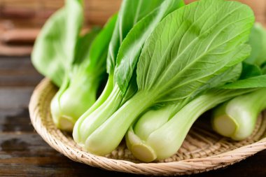 Tahta arka planda bambu sepeti içinde taze Bok Choy veya Pak Choi (Çin lahanası), organik sebzeler