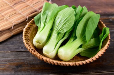 Tahta arka planda bambu sepeti içinde taze Bok Choy veya Pak Choi (Çin lahanası), organik sebzeler